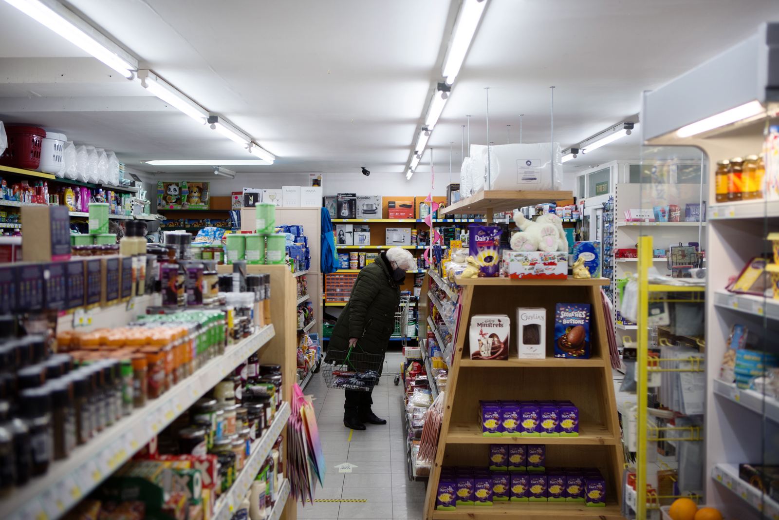 an elderly woman shops among the aisles in a well stocked local shop